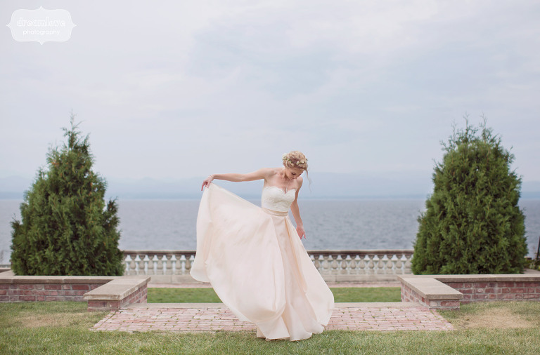 ethereal wedding photography of the bride holding up her pink skirt wedding dress in shelburne falls garden with lake champlain behind her