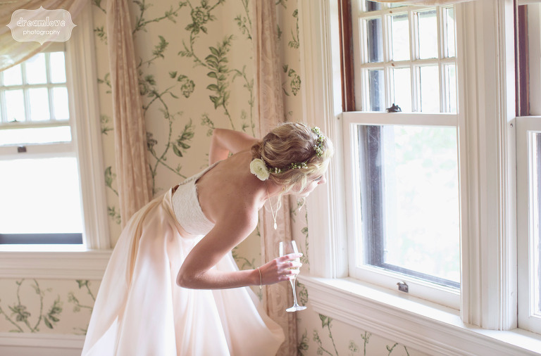 bride looks out window of shelburne farms estate while holding champagne