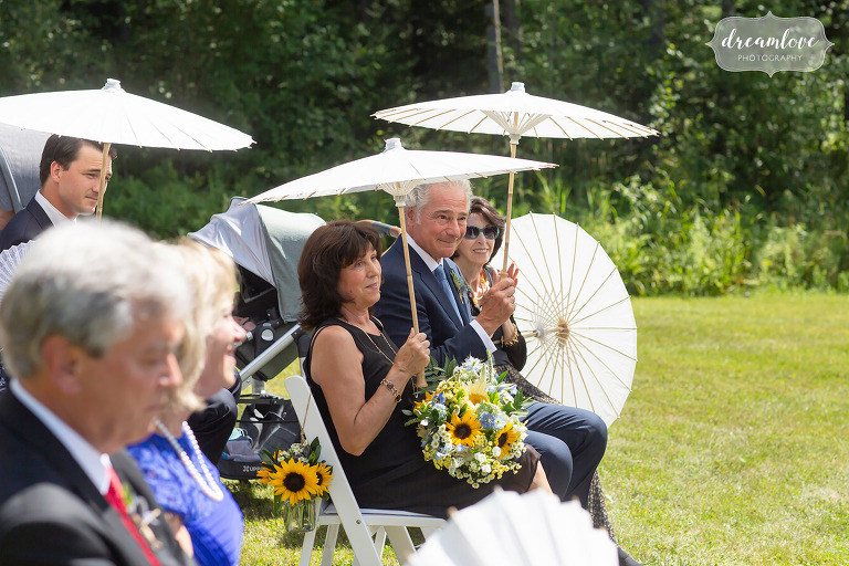 Guests hold parasols up during sunny wedding ceremony.