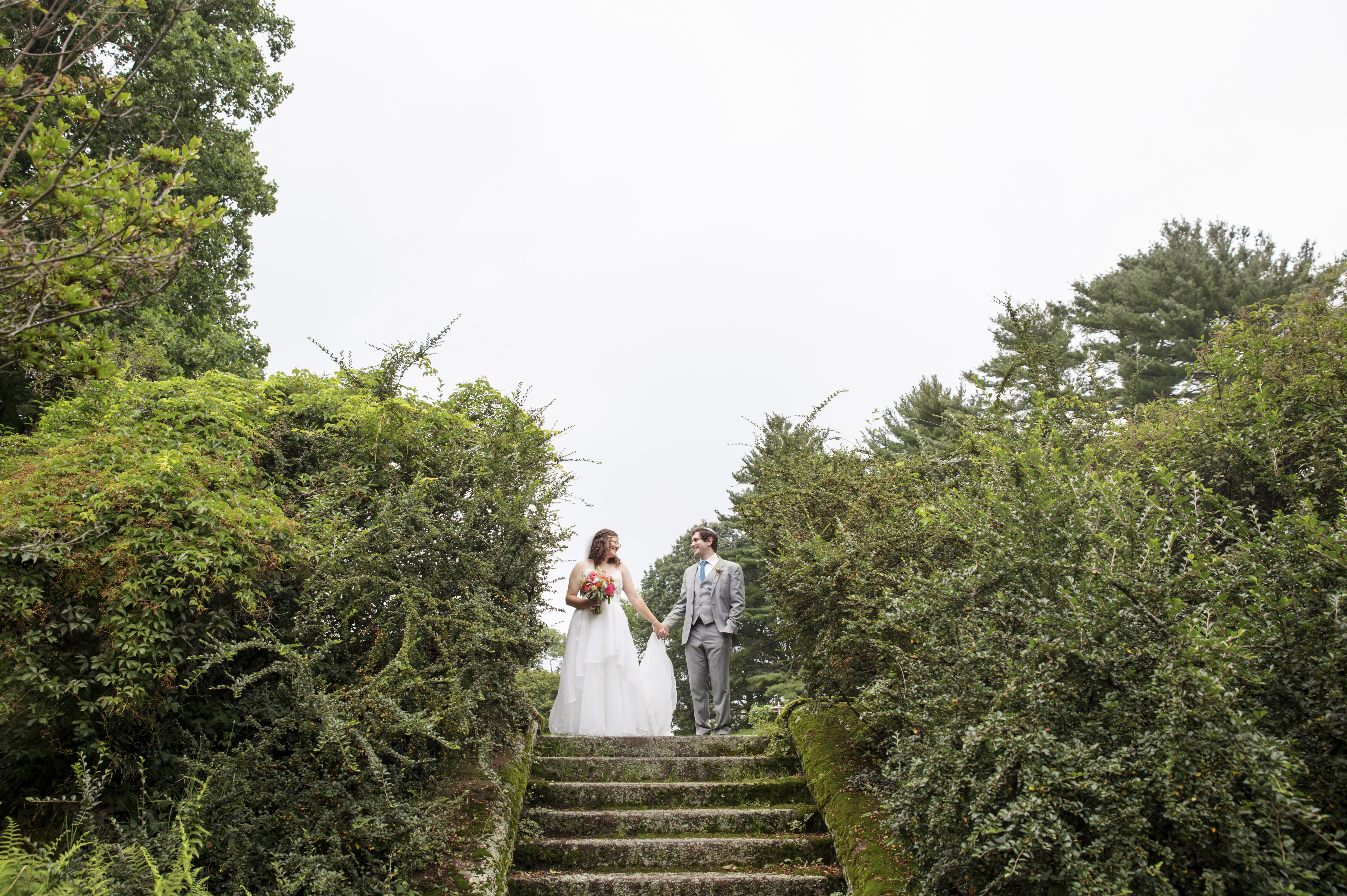 Non binary wedding couple poses at top of mossy steps at Moraine Farm.