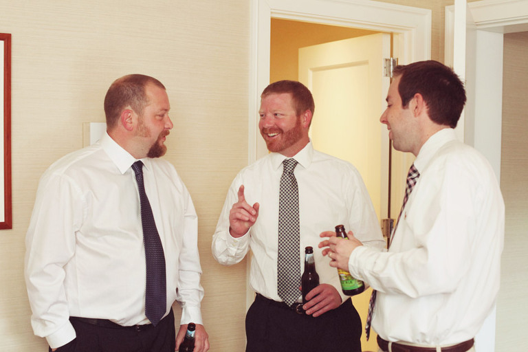 Groomsmen laugh while getting ready and drinking beer before a wedding. 