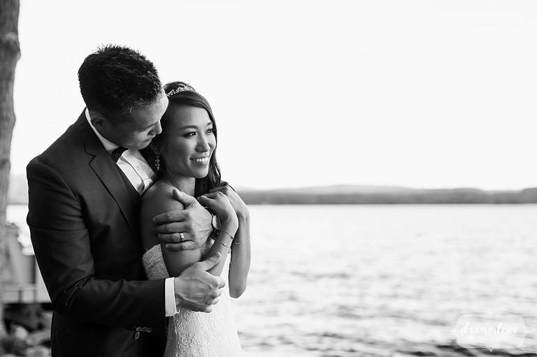 Fine art black and white photo of the bride and groom standing on the shore in Wolfeboro.