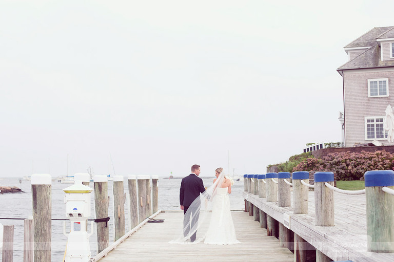 With the ocean in the background a bride and groom walk along with Wychmere's docks. 