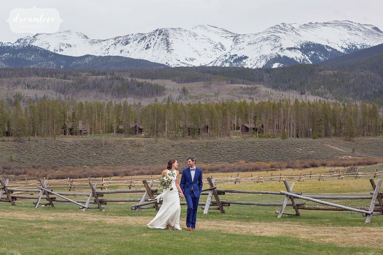 Bride and groom walk along fence at Devils Thumb Ranch near Winter Park, CO.
