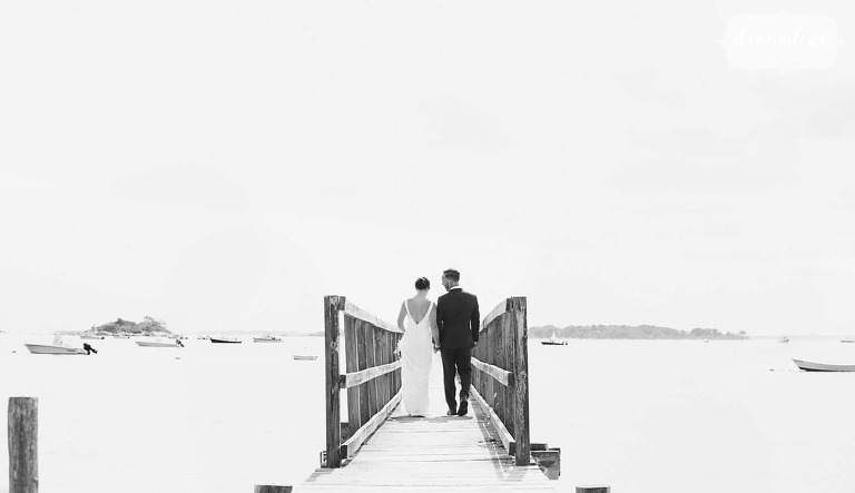 Black and white wedding photography of the bride and groom walking down the pier in Manchester, MA.