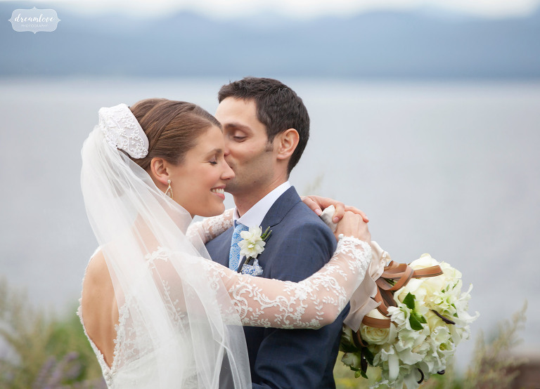 Belle mariée souriante avec les bras autour du marié et du lac Champlain en arrière-plan.
