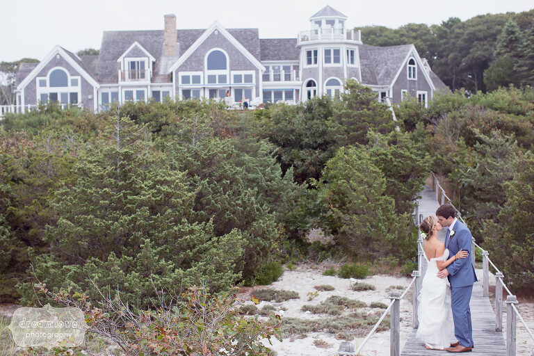 Bride and groom kissing on the boardwalk in front of a mansion on Great Island in West Yarmouth, MA.
