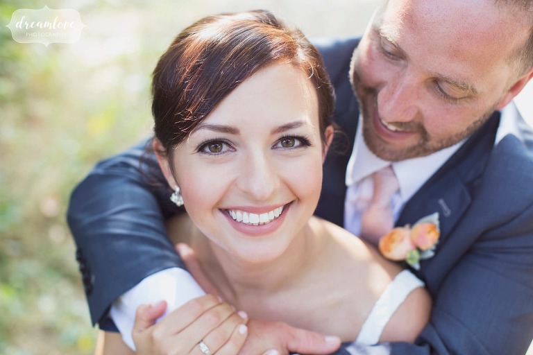 Close up photo of the bride smiling with the groom wrapping his arms around her in MA.