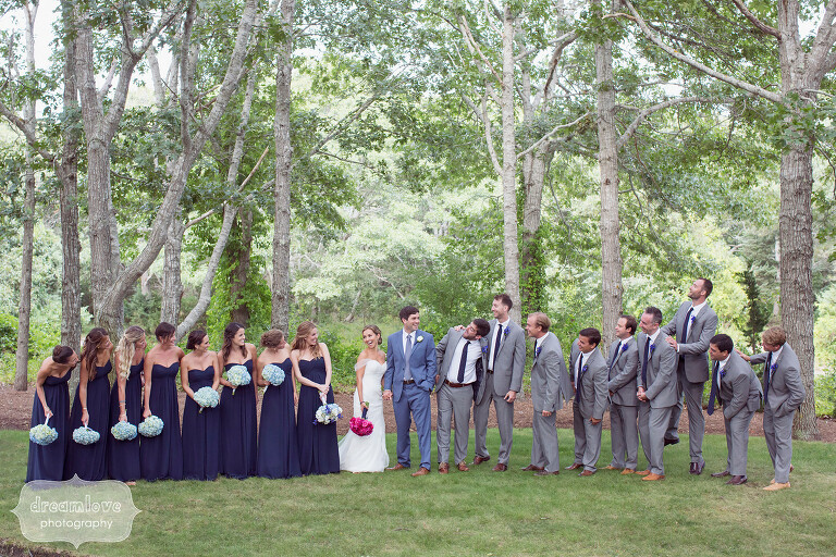 Large wedding party poses in the woods before Cape Cod wedding.