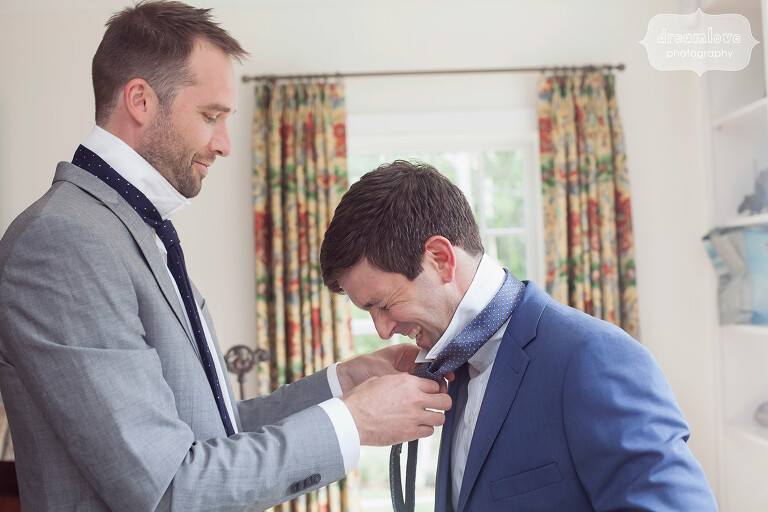 Groom laughs while putting tie on before his wedding on Cape Cod.