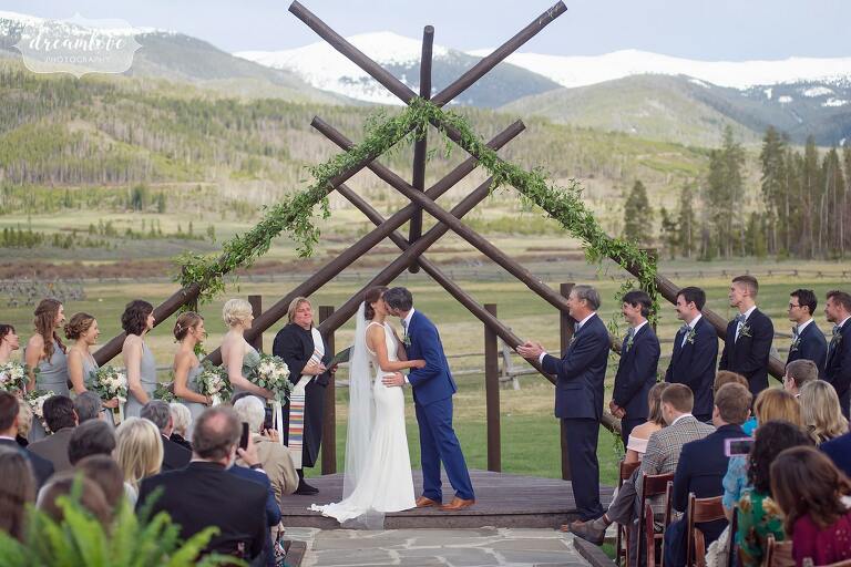Ceremony kiss with rustic timbers and scenic rocky mountains.