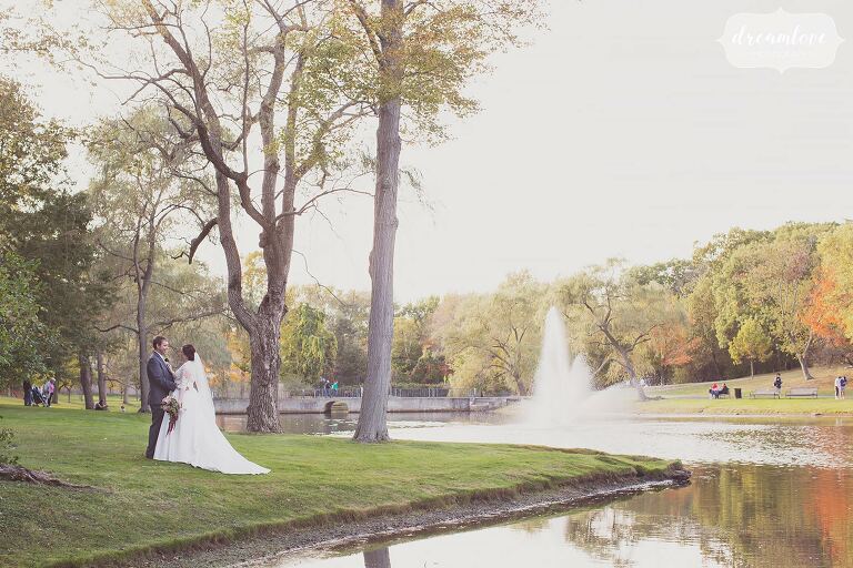 The bride and groom stand on the edge of the lake in Larz Anderson Park for their October wedding outside.