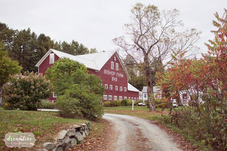 The old red dairy barn at the Bishop Farm barn wedding in the white mountains venue is pictured with a stone rock wall.