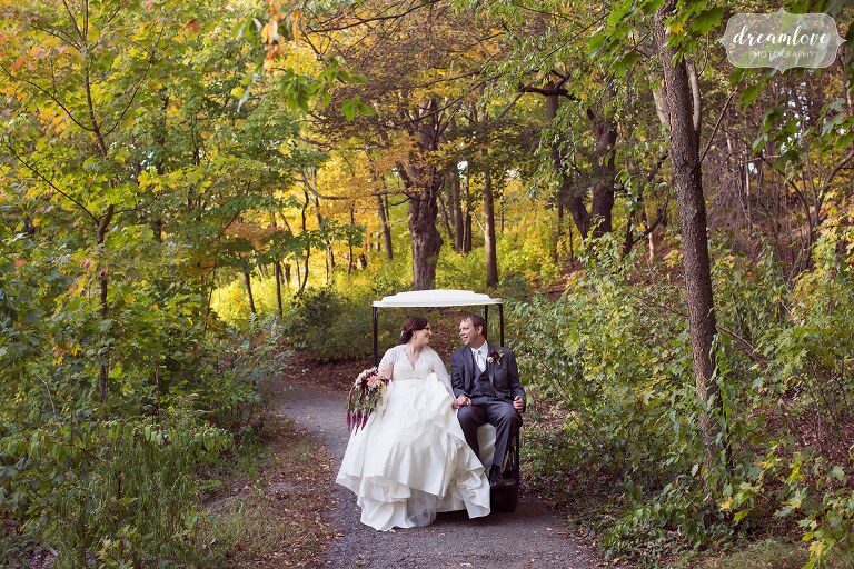 The bride and groom ride on the back of a golf cart through a tiny woodsy path at the Larz Anderson park.