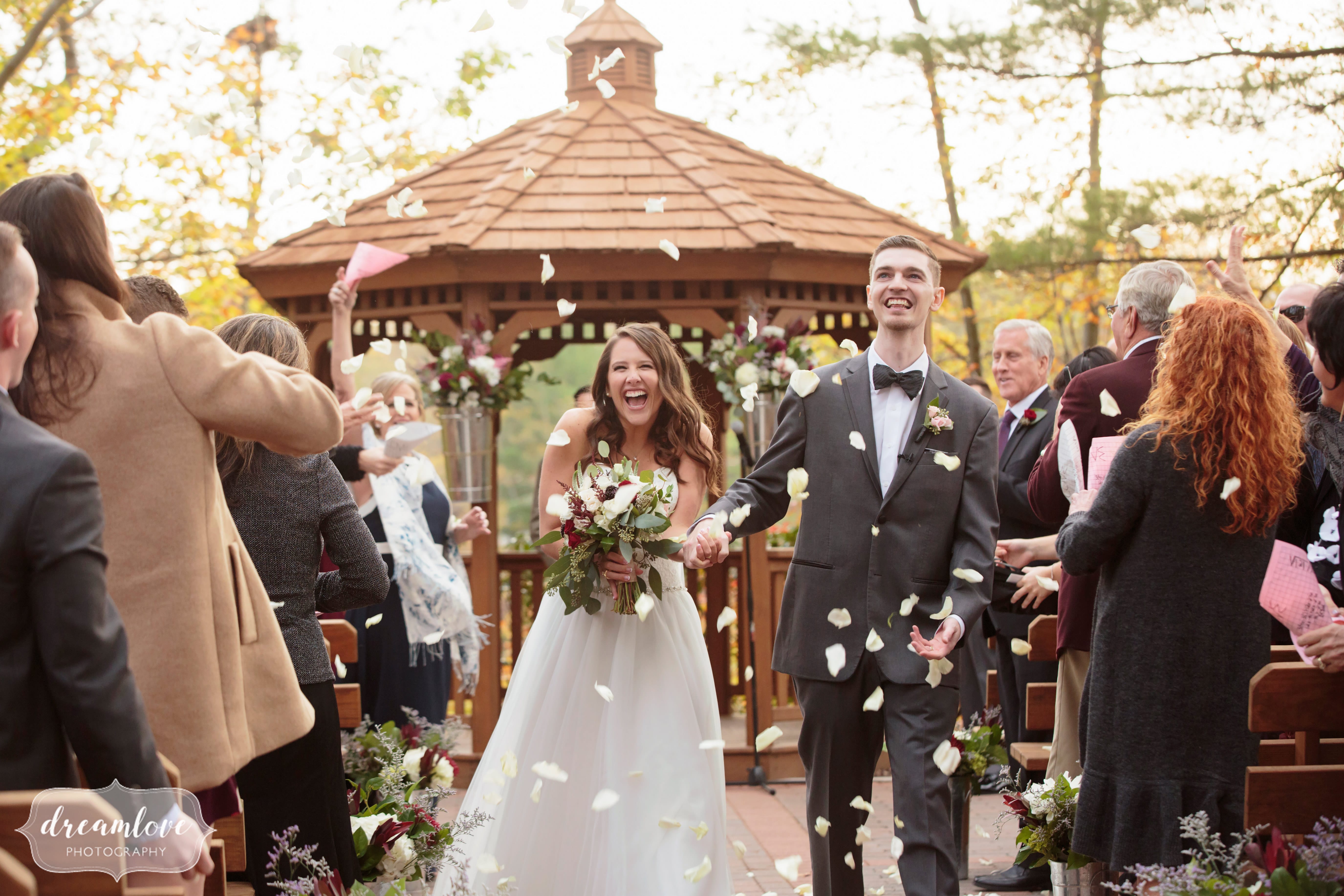 The bride and groom full of joy as they exit their wedding ceremony and guests throw flower petals around them!