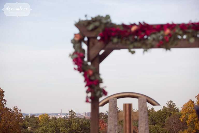 This rustic wooden ceremony arbor is draped in fall colors with the Boston skyline behind at this outdoor wedding venue called Larz Anderson.