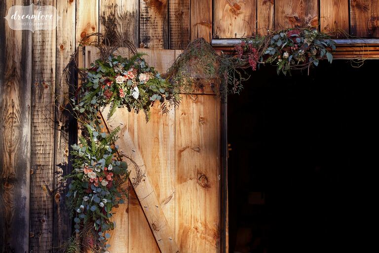 Romantic and thick floral garland with greenery is draped over the barn door at the Gould Barn.