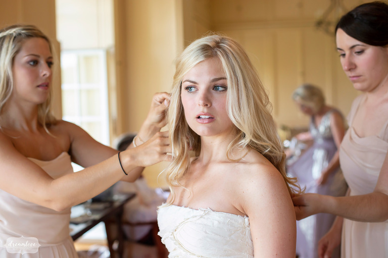 Beautiful bride with blond hair in strapless dress has hair fixed in a yellow room.