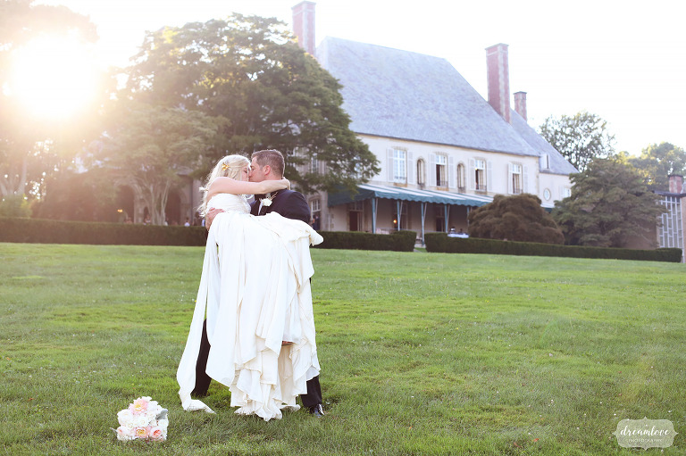 Le marié soulève la mariée derrière le lieu de mariage Glen Manor House sur la côte RI.