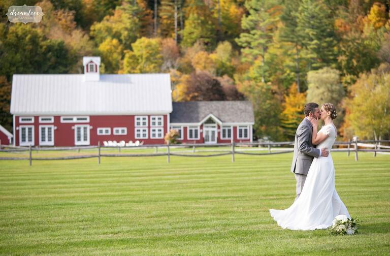 Bride and groom kiss in a field with red Riverside Farm barn behind them.