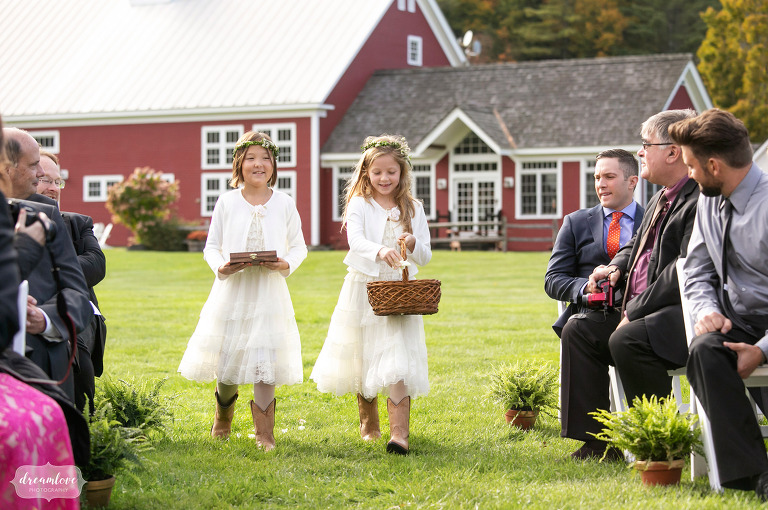 Two flower girls walk in front of a red barn.