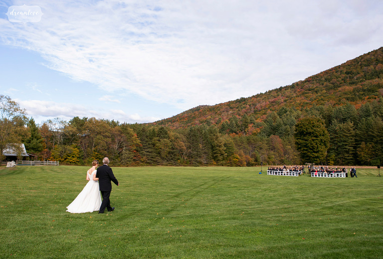 Bride and her father walk through field into outdoor ceremony space at Riverside Farm.