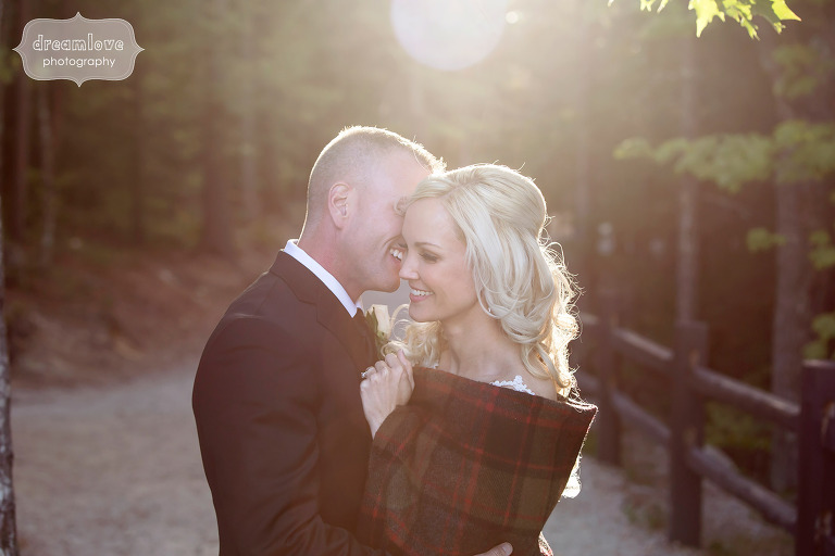 Bride wrapped in a plaid blanket is hugged by the groom at the Cathedral Ledge in NH during September wedding.