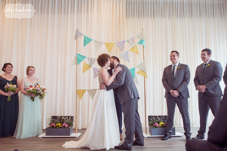 Bride and groom kiss at the end of their ceremony with a colorful pennants backdrop on Cape Cod.