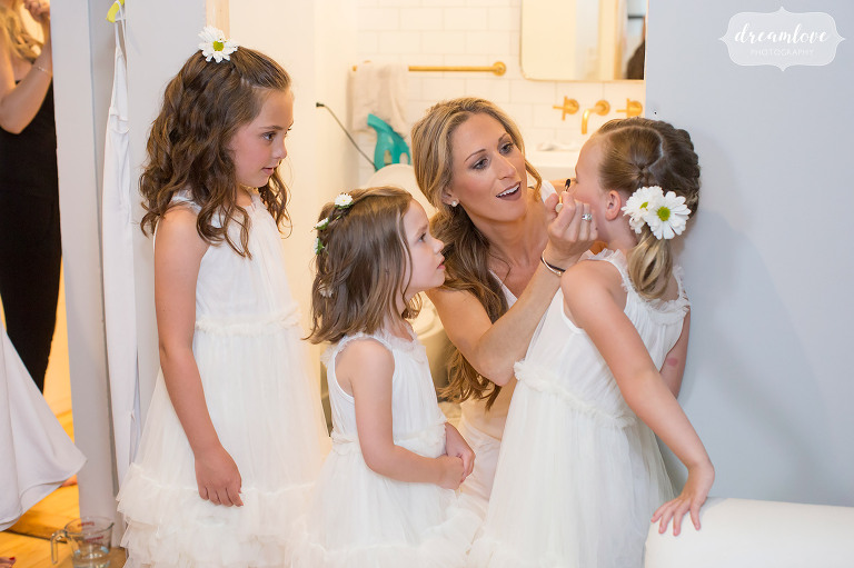 Documentary wedding photo of the bride helping her flower girls put on makeup before her Stowe, VT wedding.