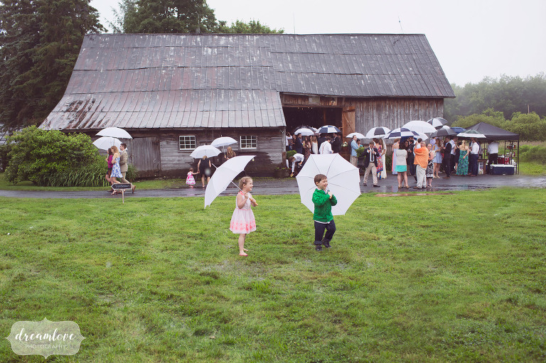 Kids holding umbrellas in front of the Stowe Comfort Farm on a rainy wedding day.