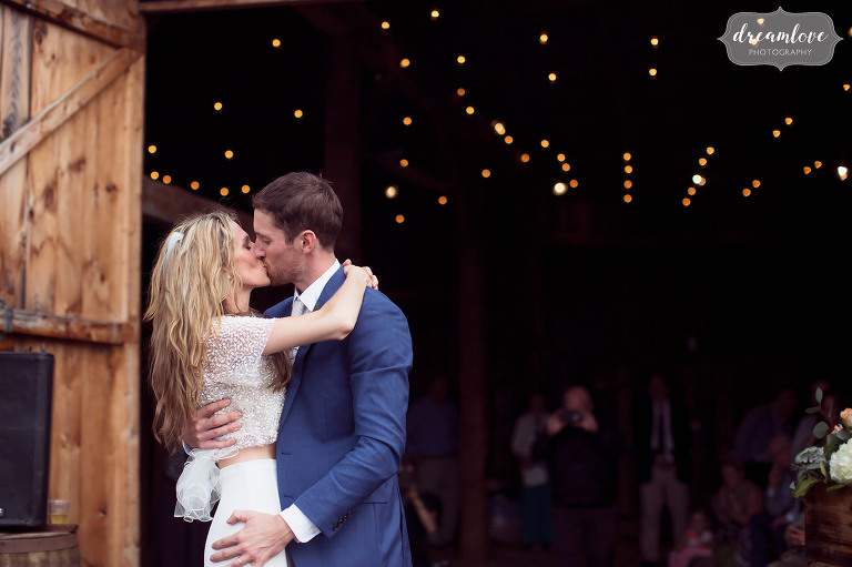 The bride and groom kiss during their first dance in the rain with twinkle lights behind them.