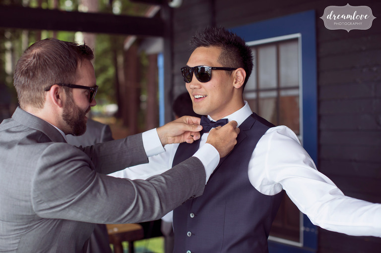 A groomsman helps out this charismatic groom by tying his bowtie before his backyard wedding on Lake Wentworth in Wolfeboro, NH.