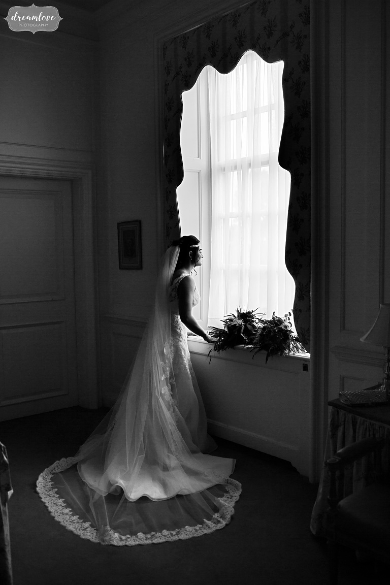 The bride looks out of the very large windows in the bridal suite at the Crane Estate.