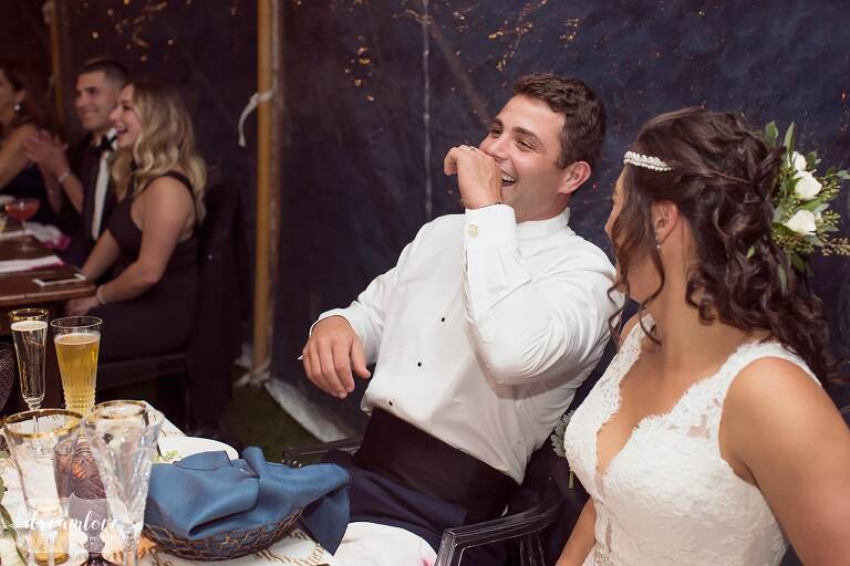 The groom laughs during the father of the bride's toast.