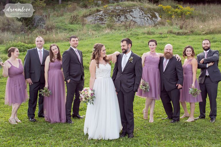 The wedding party in lilac and dark gray gathers in a field at the Warfield House Inn.
