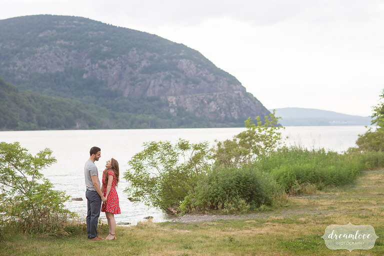 Couple holds hands during Hudson Valley engagement photos in front of Storm King Mountain in Cold Spring.