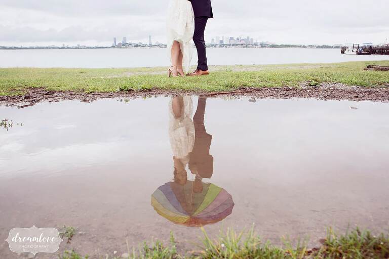 Artistic wedding photo of the bride and groom reflected in a puddle with Boston skyline behind them.