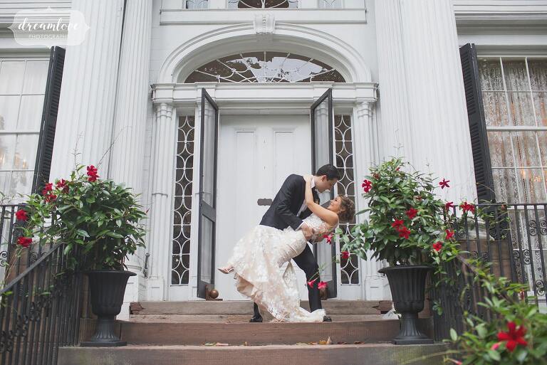 The bride and groom have a Hollywood kiss in front of the Linden Place mansion.