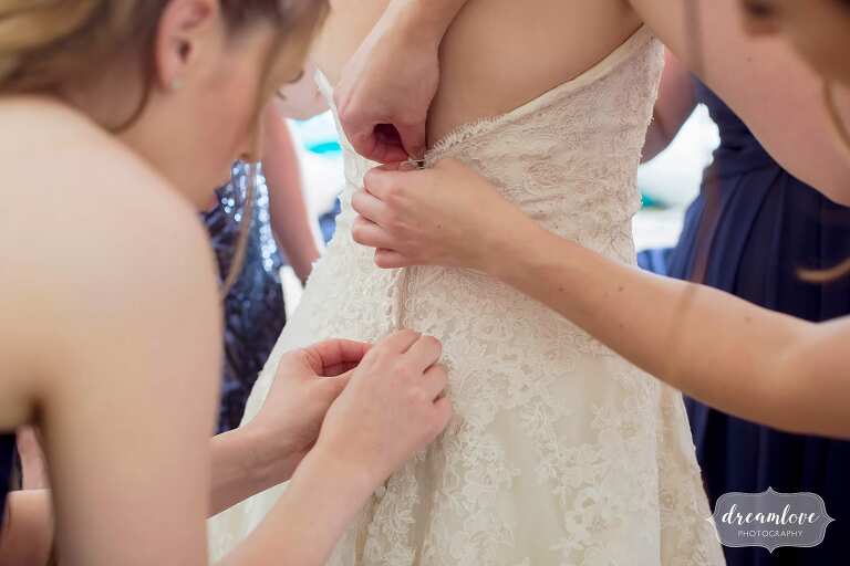 The bridesmaids all pitch in to help button the bride's wedding dress.