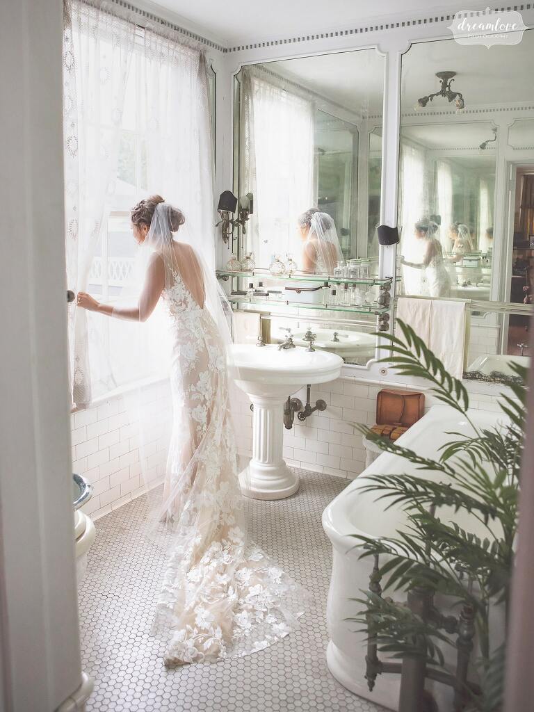 Bride looks out of the window in an antique bathroom at the Linden Place in RI.