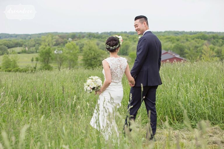 Bride and groom walking through field by Hudson Valley wedding photographer.
