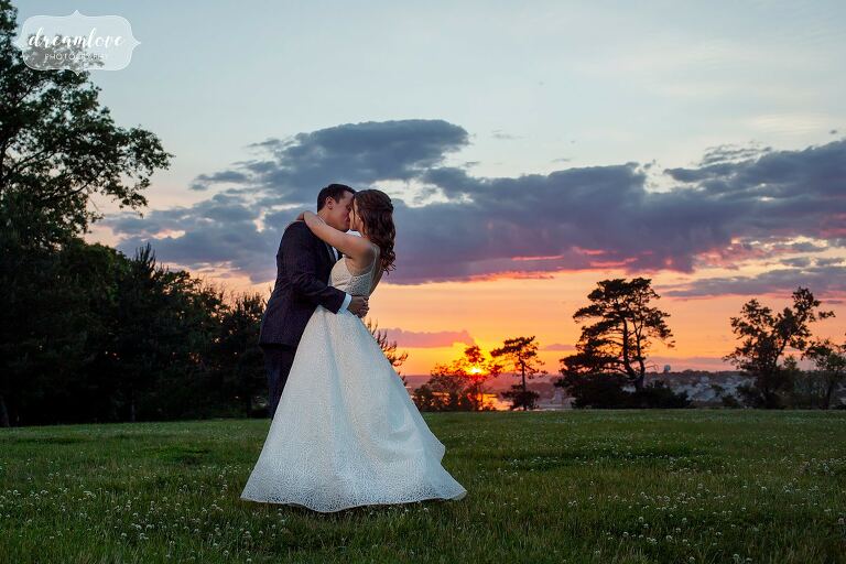 Bride and groom embrace with sunset behind them over the ocean at the Crane Estate.