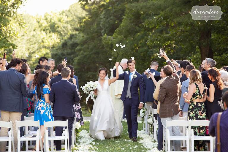 Bride and groom exit ceremony while guests throw flower petals.