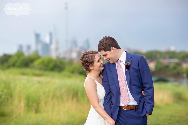 Bride and groom stand in front of the Philly skyline at their Bartram's Garden Wedding.