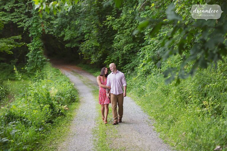 Couple walks along a path in southern Vermont during summer engagement photo session.