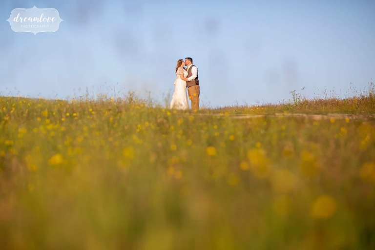 Bride and groom pose in a field of wildflowers on the summit of Mt. Greylock at sunset.