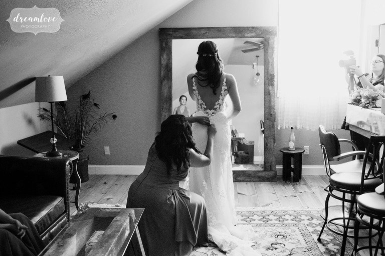 Bridesmaid helps the bride get her dress on before her NH barn wedding.
