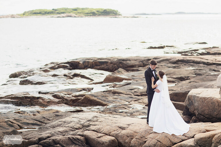 Bride and groom stand on rocks at Magnolia Beach in Gloucester, MA.
