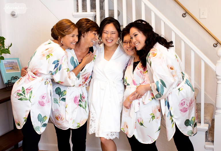 Five bridemsaids in floral robes cuddle before wedding.