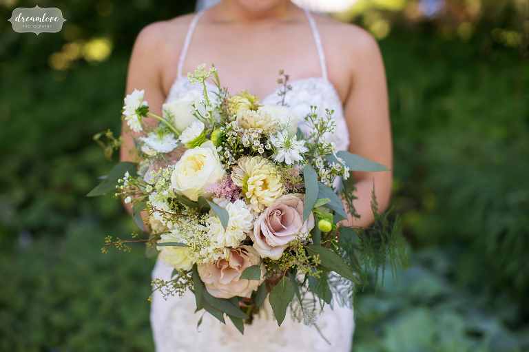 Bride holds large pastel floral bouquet with roses and greenery.